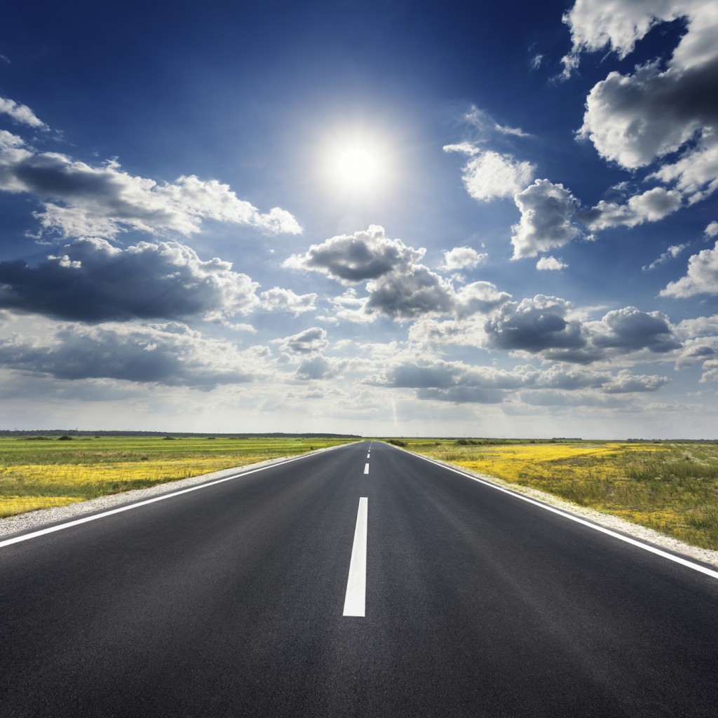 Driving on an empty asphalt road through the agricultural fields at idyllic sunny day towards the sun.