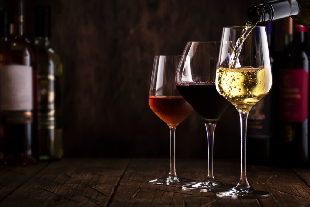 Wine tasting. Whte wine pouring into glass on background with selection of red, white and rose wines in glasses and bottles